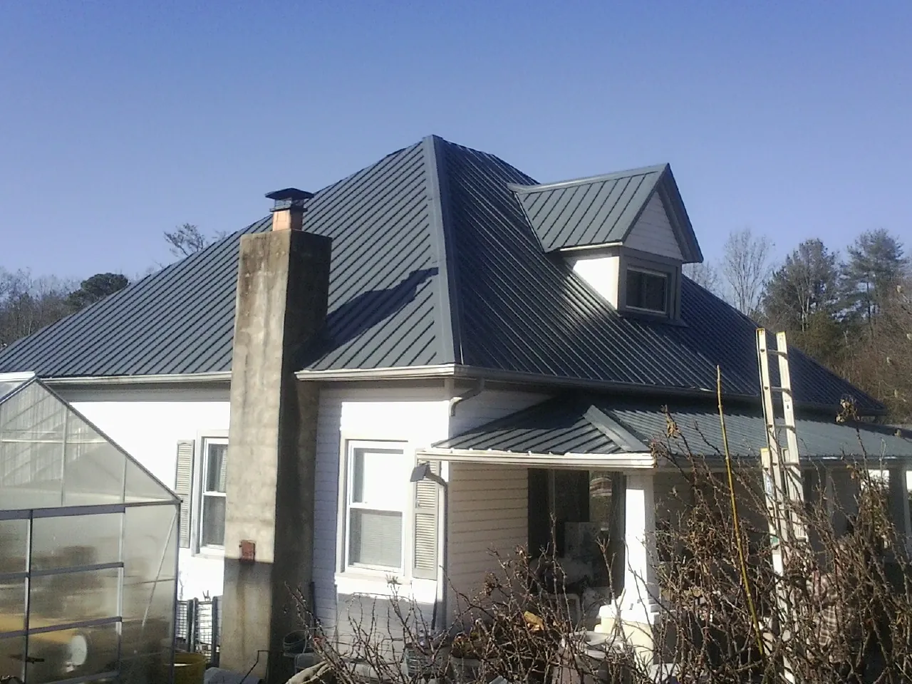 Dark blue standing seam metal roof on a white farmhouse with dormer — Slate & Tile Roof Repair by Roofing Brothers in Crofton