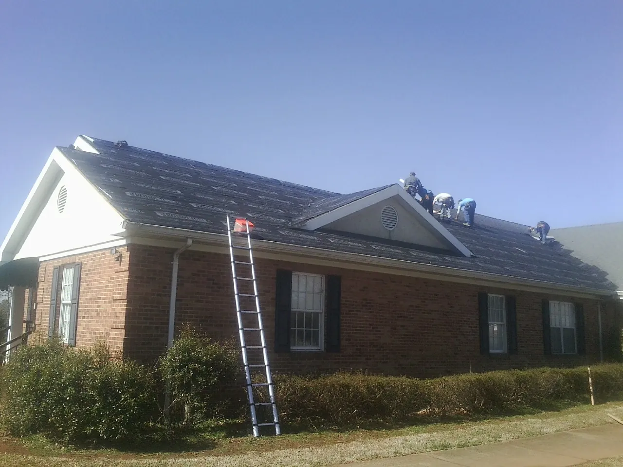Crew tearing shingles off a brick ranch roof with a ladder set — Emergency Roof Repair work by our crew in Crofton