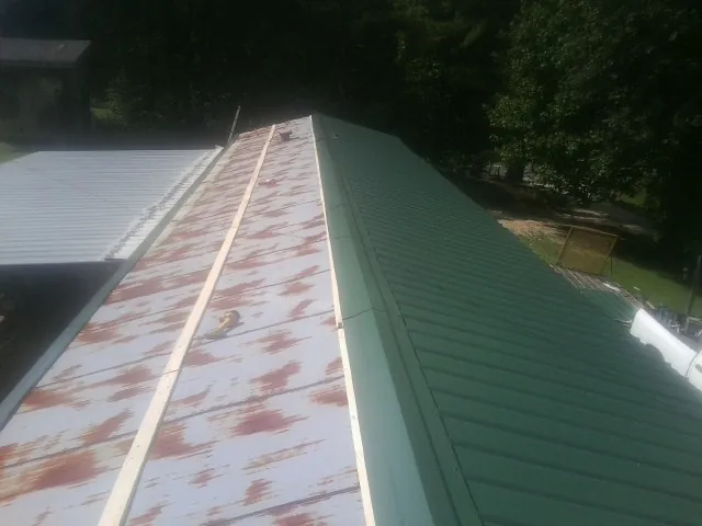 Old rusted panels beside newly installed green metal roofing — Wind Damage Roof Repair by Roofing Brothers in Crofton
