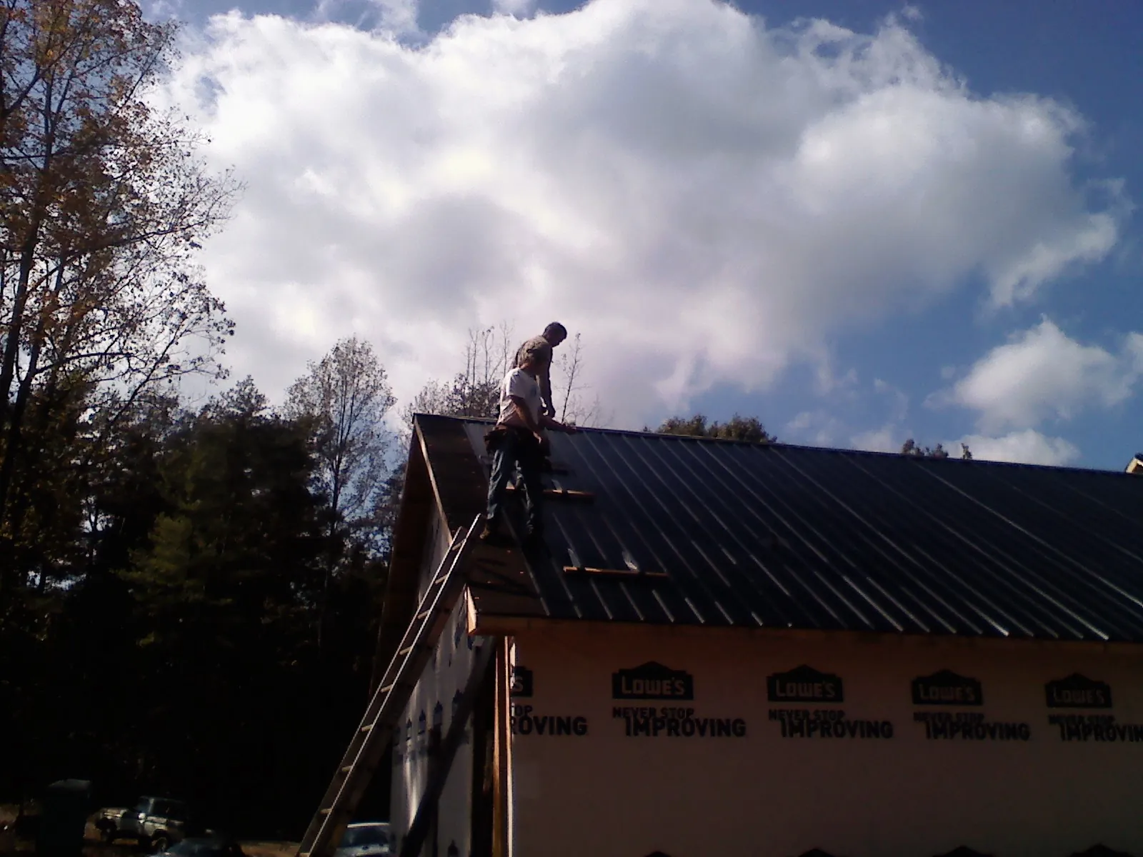 Roofer fastening dark metal panels high against a cloudy sky, from a Roof Inspection job in Crofton
