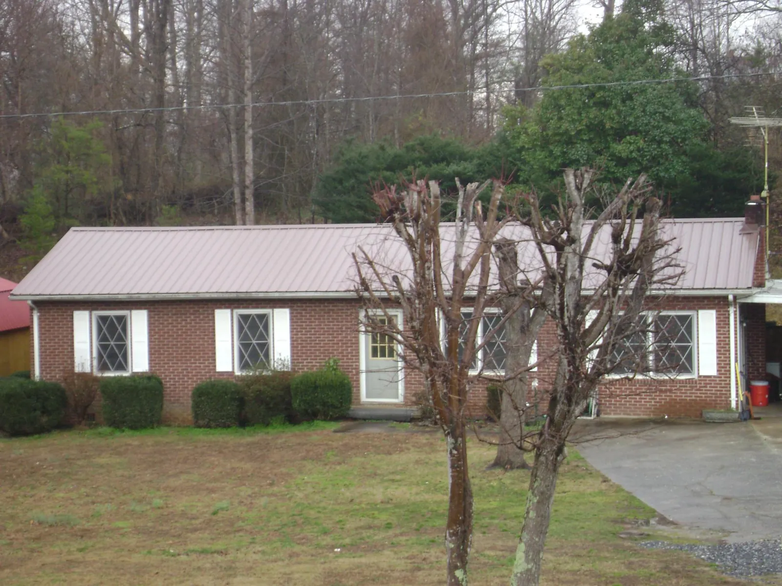 Mauve metal roof on a brick ranch home behind bare trees in Crofton